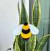 image of a fused bumble bee with two antennas glued to a plant stake.  the bee plant stake is shown in front of a snake plant