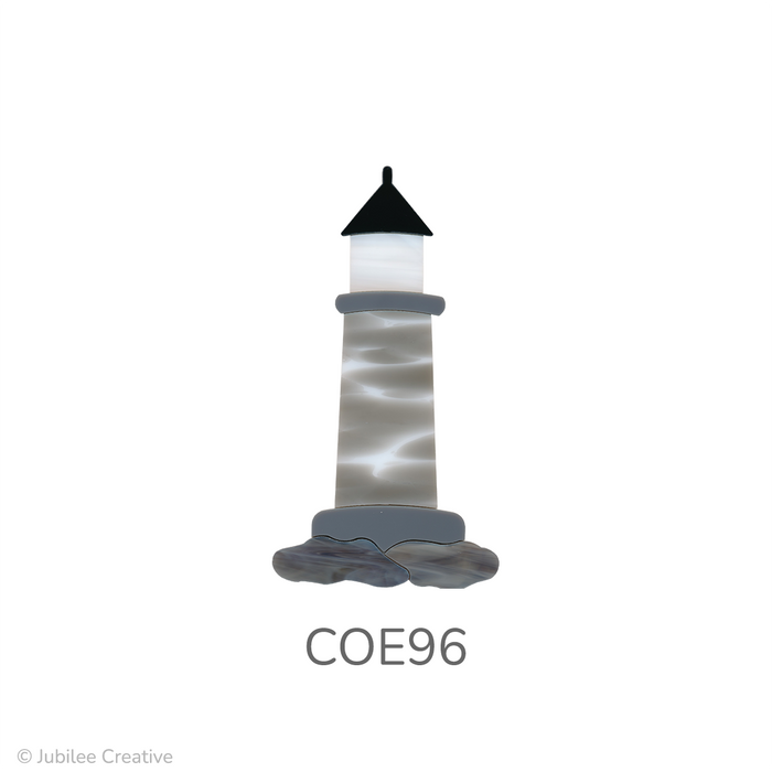 image of a fusible precut glass lighthouse. It features a black roof, white window, gray building, and brown-gray rocks - COE96